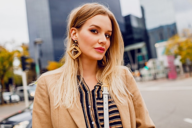 Bouchent Le Portrait D'une Femme Blonde élégante Avec Des Boucles D'oreilles élégantes. Dame élégante Bénéficiant De Loisirs Près Du Centre Commercial Dans Une Grande Ville Moderne.