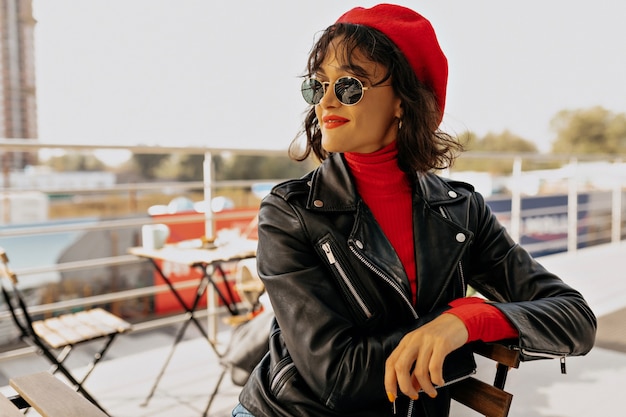 Bouchent le portrait d'une femme charmante élégante en béret rouge avec des lèvres rouges assis sur une terrasse extérieure