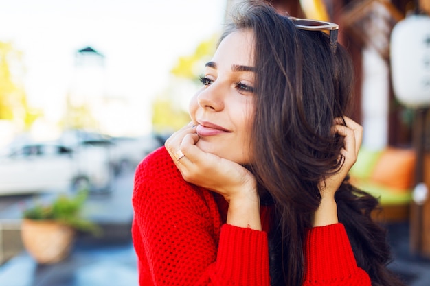 Bouchent le portrait d'une femme romantique élégante avec des cheveux ondulés brune avec des lunettes de soleil rétro élégantes et un pull tricoté. Femme se détendre dans un café moderne le matin et boire du café.