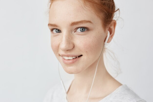 Bouchent le portrait de femme rousse avec des taches de rousseur dans les écouteurs en souriant.