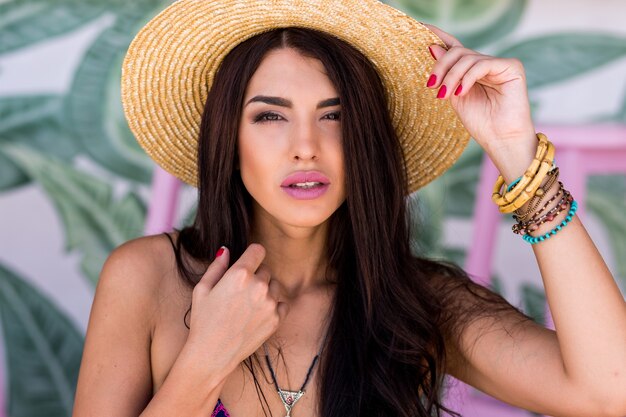 Bouchent le portrait d'une femme sensuelle au chapeau de paille avec de longs poils parfaits posant au bar de la plage. Ambiance estivale.