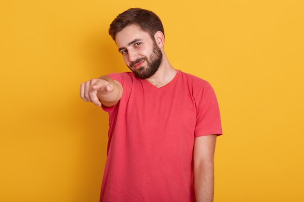 Bouchent portrait d'heureux jeune homme pointant sur la caméra et souriant tout en portant un t-shirt décontracté rouge