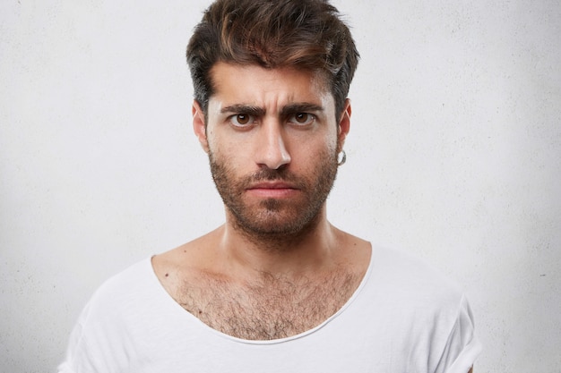 Photo gratuite bouchent le portrait d'un homme barbu sombre et sérieux avec une coiffure élégante. beau mec aux yeux noirs fronçant les sourcils montrant son insatisfaction