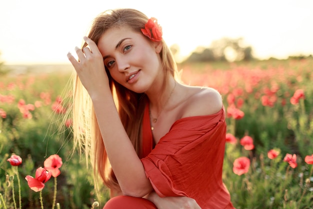 Bouchent le portrait de jeune femme aux cheveux longs souriante marchant dans un champ de pavot dans la soirée. Couleurs chaudes du coucher du soleil.