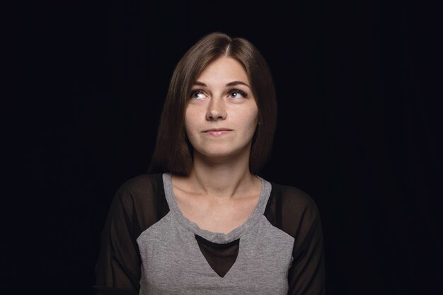 Bouchent le portrait de jeune femme isolée sur fond noir de studio. Photoshot des émotions réelles du modèle féminin. Rêver et souriant, plein d'espoir et heureux. Expression faciale, concept d'émotions humaines.