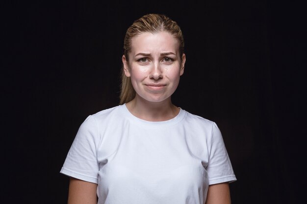 Bouchent le portrait de la jeune femme isolée sur le mur noir. vraies émotions du modèle féminin. Pleurer, triste, triste et sans espoir. Expression faciale, concept d'émotions humaines.