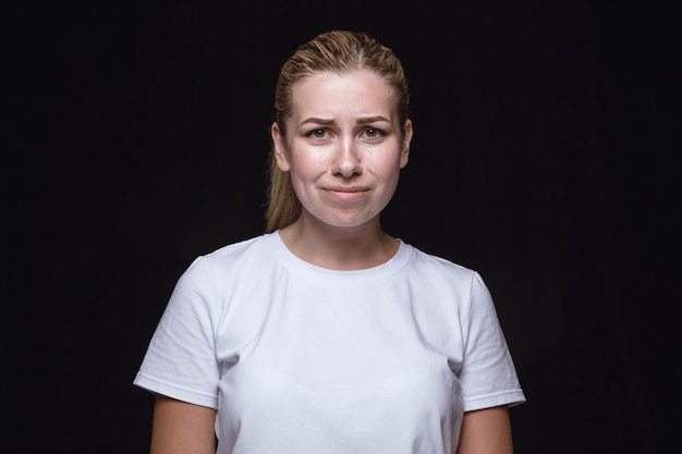 Bouchent le portrait de la jeune femme isolée sur le mur noir. vraies émotions du modèle féminin. Pleurer, triste, triste et sans espoir. Expression faciale, concept d'émotions humaines.