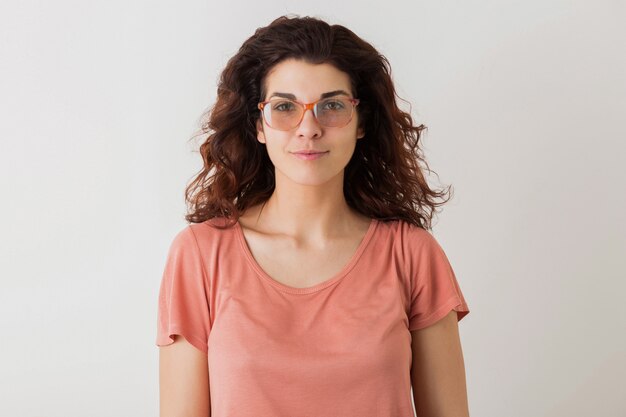 Bouchent le portrait de jeune femme jolie naturelle avec une coiffure frisée en chemise rose posant portant des lunettes isolées