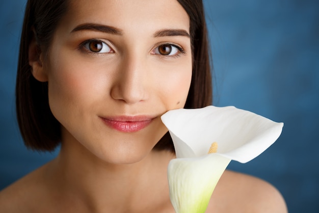 Bouchent portrait de jeune femme tendre avec fleur blanche sur mur bleu