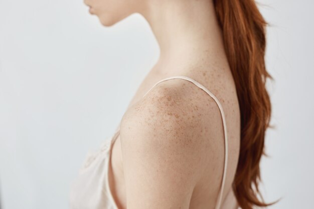 Bouchent le portrait de jeune fille tachetée de rousseur tendre jeune en lingerie sur mur blanc.