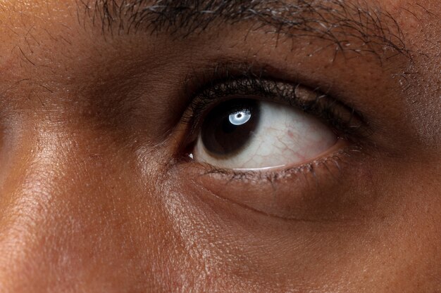 Bouchent le portrait de jeune homme afro-américain sur fond bleu. Émotions humaines, expression faciale, publicité, vente ou concept de beauté. Photoshot d'un œil. Il a l'air calme, levant les yeux.