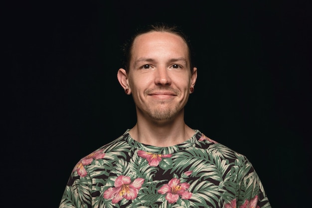 Bouchent le portrait de jeune homme isolé sur fond noir de studio. Photoshot des vraies émotions du modèle masculin. Sourire, se sentir heureux. Expression faciale, concept d'émotions humaines pures et claires.