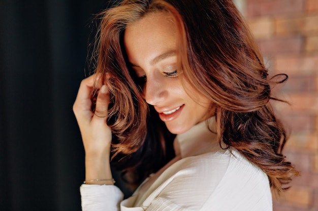 Bouchent le portrait de jolie femme européenne aux cheveux bouclés posant sur un mur noir et souriant