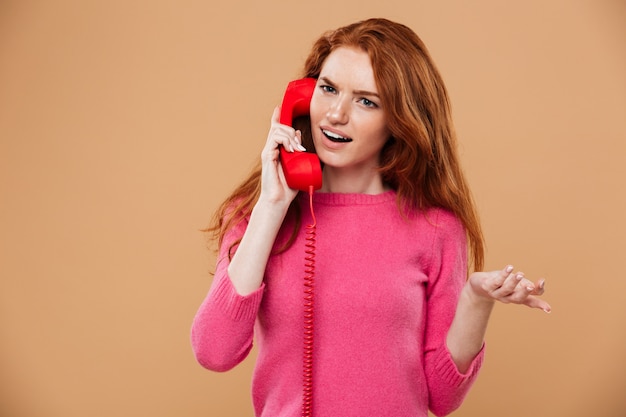 Bouchent le portrait d'une jolie rousse confuse parler par téléphone rouge classique