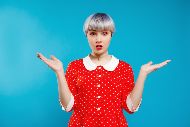 Photo gratuite bouchent portrait me demandant belle fille de poupée avec de courts cheveux violet clair portant une robe rouge sur le mur bleu