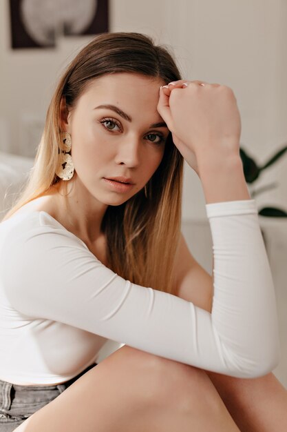 Bouchent le portrait de la merveilleuse femme européenne aux cheveux blonds regardant la caméra au soleil en studio blanc moderne