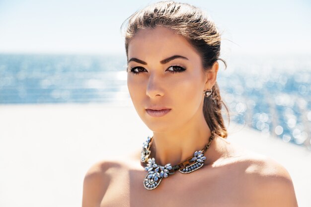 Bouchent le portrait de mode de la belle jeune femme en élégant gros collier de diamants posant son bord de mer. Couleurs claires et claires.