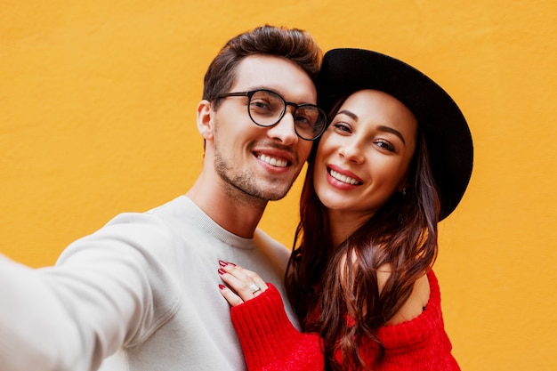 Bouchent le portrait de mode de vie de fille heureuse avec son petit ami faisant autoportrait par téléphone mobile. mur jaune. Porter un pull en tricot rouge. Ambiance de fête du nouvel an.