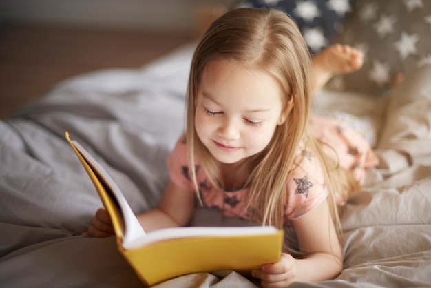 Photo gratuite bouchent le portrait de petite fille lisant dans son lit