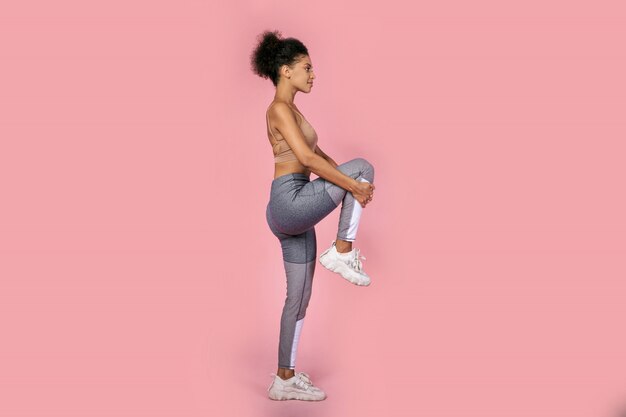 Bouchent le portrait en studio de la belle femme noire aux cheveux afro, faire des exercices en studio sur fond rose. Longueur totale.