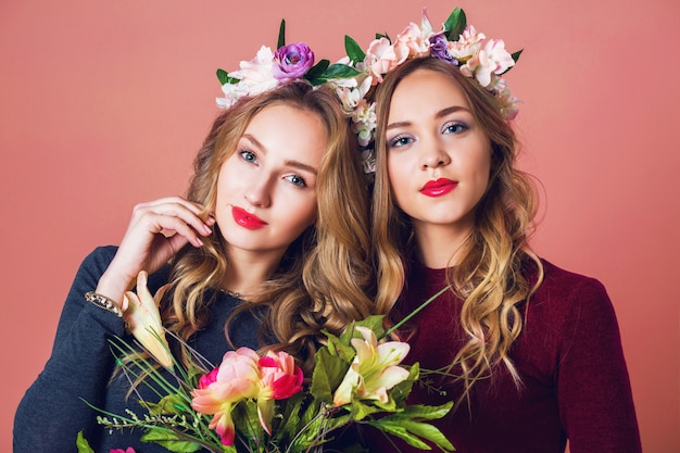 Bouchent le portrait en studio de deux jeunes femmes jolies blondes en colère de fleurs de printemps, incroyable coiffure longue ondulée, maquillage lumineux, regardant la caméra.