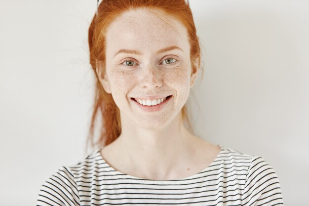 Bouchent le portrait très détaillé d'une étudiante caucasienne heureuse et joyeuse avec un sourire mignon, des cheveux roux et une peau parfaite de taches de rousseur saine se reposant à l'intérieur après des conférences à l'université