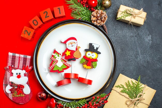 Bouchent la vue de l'assiette à dîner accessoires de décoration branches de sapin et numéros chaussette de Noël sur une serviette rouge à côté de cadeau sur une table noire