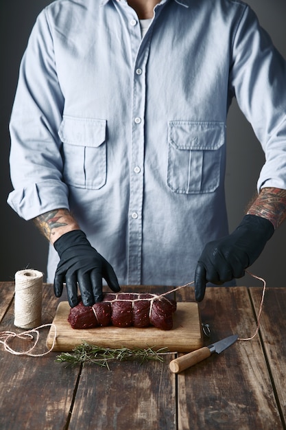 Photo gratuite le boucher attache la viande avec une corde pour fumer, sur la table avec des espèces