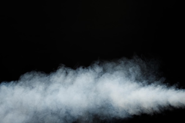 Bouffées denses et moelleuses de fumée blanche et de brouillard sur fond noir, nuages de fumée abstraits, mouvement flou flou. fumer souffle de la machine à glace carbonique voler et flotter dans l'air, texture d'effet