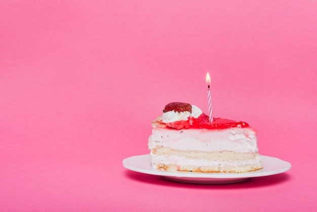 Bougie lumineuse sur la tranche de gâteau d&#39;anniversaire avec fond rose