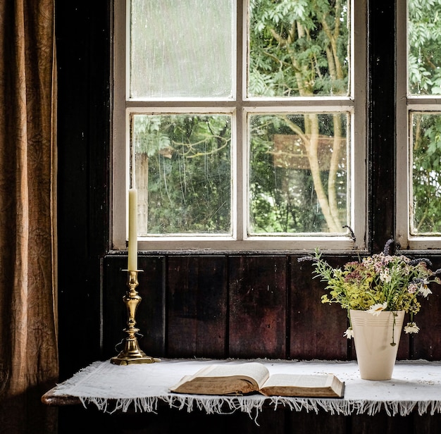 Photo gratuite bougie posée à côté des fleurs et un livre devant la fenêtre