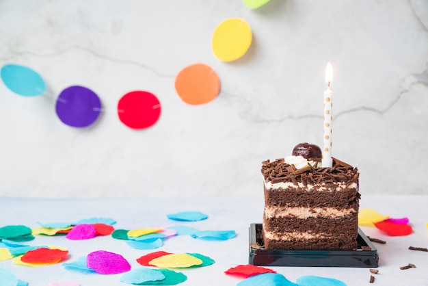 Photo gratuite bougie sur la tranche de gâteau et confettis sur table