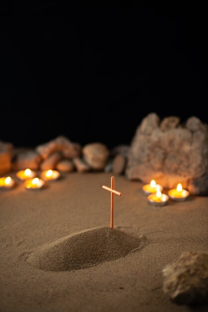 Des bougies allumées avec des pierres et une petite tombe sur une surface sombre de sable