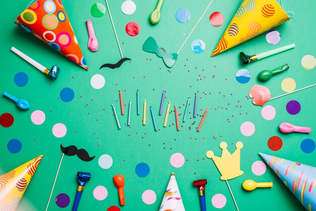 Bougies colorées entourées de chapeaux de fête; des ballons; accessoires d&#39;anniversaire et confettis sur fond vert