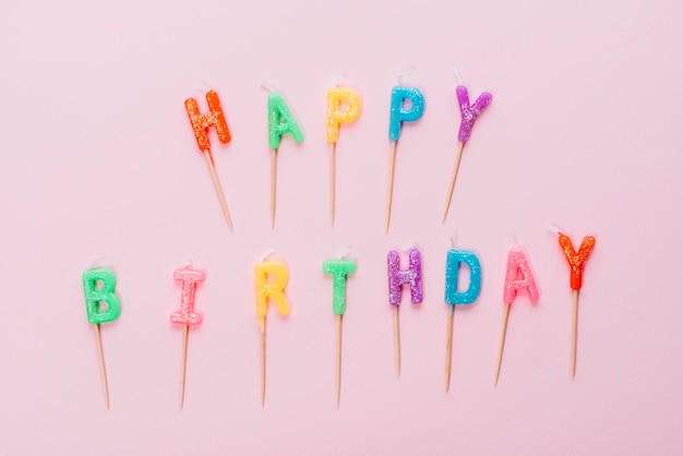 Bougies colorées joyeux anniversaire avec un bâton sur fond rose