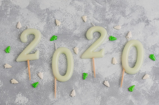 Des bougies en forme de nombre 2020 comme symbole de la nouvelle année à côté des bonbons scintillants en forme de noël sur une table grise. vue de dessus, plat poser