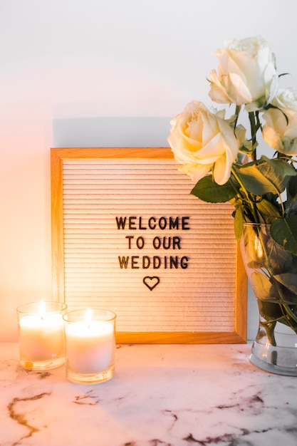 Des bougies lumineuses près du tableau de bienvenue du mariage et un vase sur fond blanc