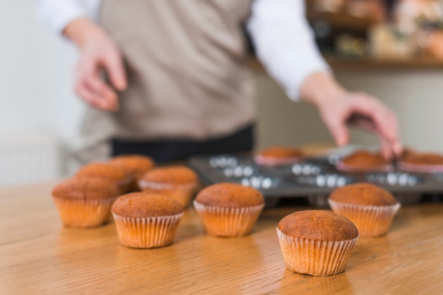 Photo gratuite boulanger femme floue enlever les muffins du plateau sur la table en bois texturé