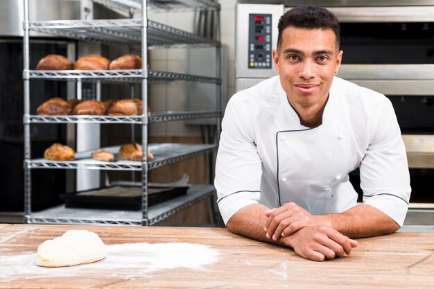 Boulanger mâle debout derrière la table avec de la pâte à la boulangerie