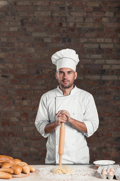 Boulanger mâle debout derrière la table avec de la pâte; Ingrédients; et pain cuit