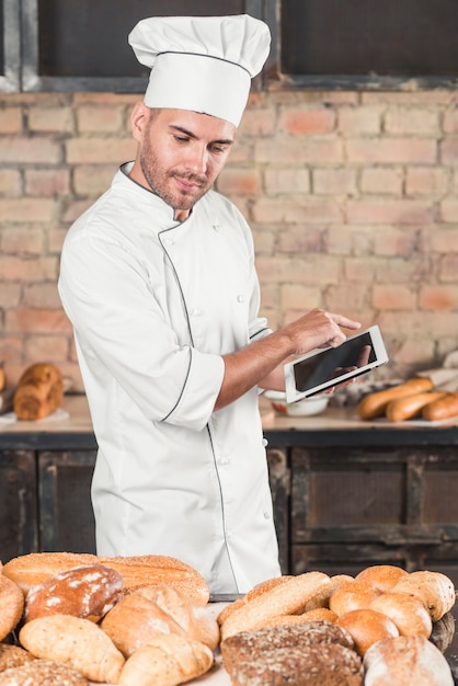 Boulanger mâle regardant assortiment de pains à l'aide d'une tablette numérique