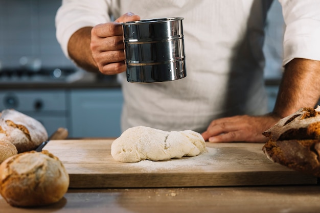 Boulanger mâle tamiser la farine de blé à travers un tamis en acier sur la pâte à pétrir