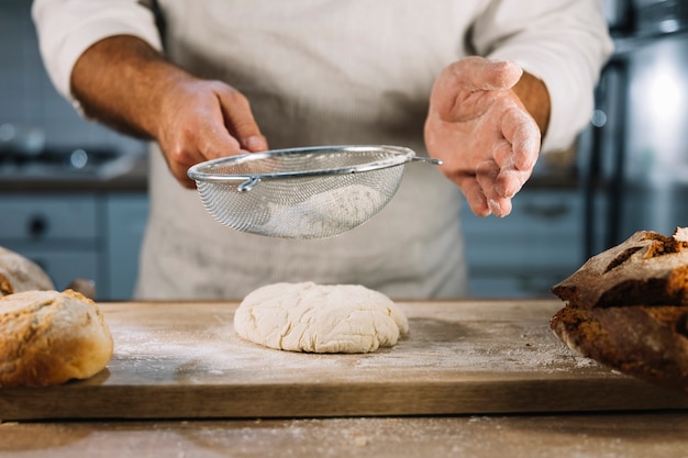 Boulanger mâle tamiser la farine de blé à travers un tamis en acier sur la pâte à pétrir