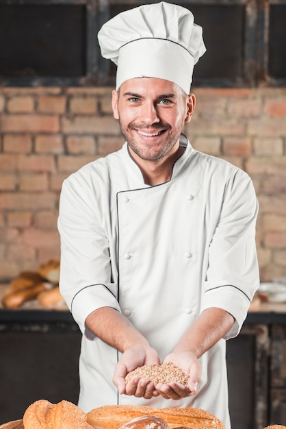 Boulanger mâle tenant une poignée de grains de blé sur le pain cuit