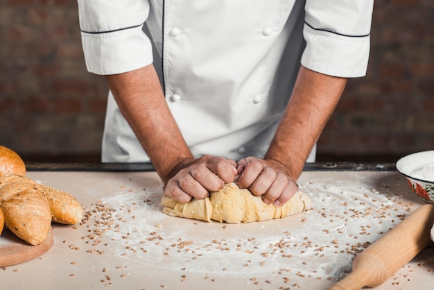 Boulanger mâle en train de pétrir la pâte sur le plan de travail de la cuisine