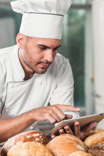 Boulanger mâle utilisant une tablette numérique avec du pain