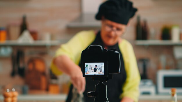 Boulangerie de la vieille dame présentant une recette de cuisine sur le podcast de cuisine de la cuisine. Chef influenceur blogueur à la retraite utilisant la technologie Internet pour communiquer, bloguer sur les réseaux sociaux avec un équipement numérique