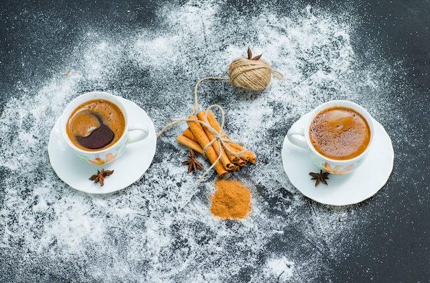 Une boule de corde attachée à la cannelle sèche avec de la cannelle en poudre et deux tasses de café vue grand angle sur la surface texturée grise