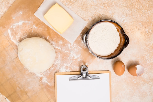 Boule de pâte; farine; bloc de beurre; oeufs et presse-papiers sur fond de cuisine