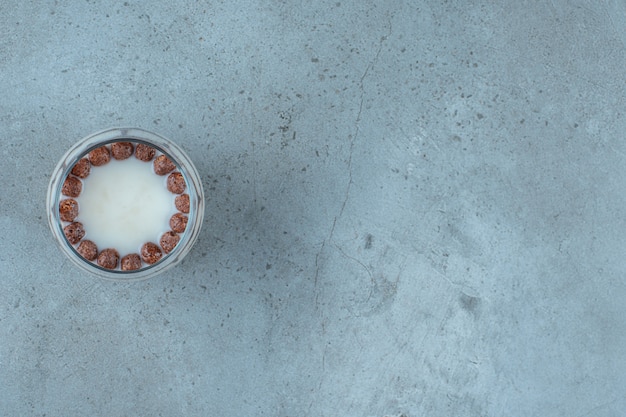 Boules de chocolat dans un verre de lait, sur fond bleu.